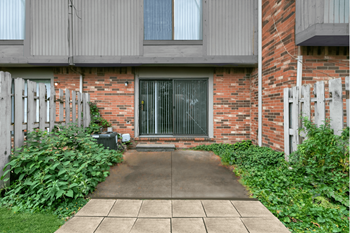 A brick building with a grey door and a concrete walkway leading to it